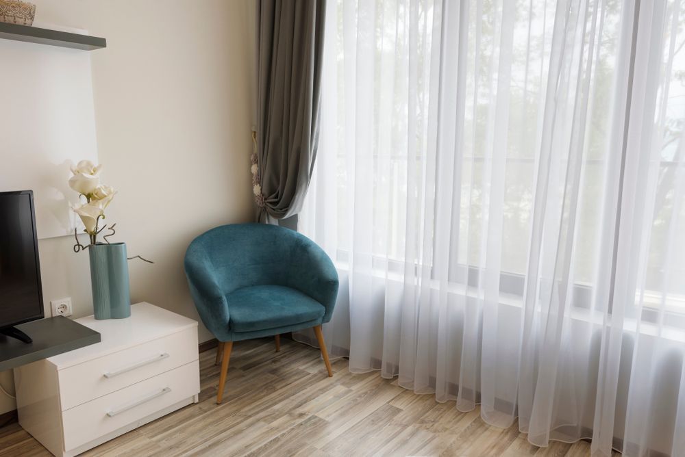 A Living Room With a Blue Chair, a Television, a Nightstand and a Window — Catrina's Custom Curtains & Blinds in Toukley, NSW