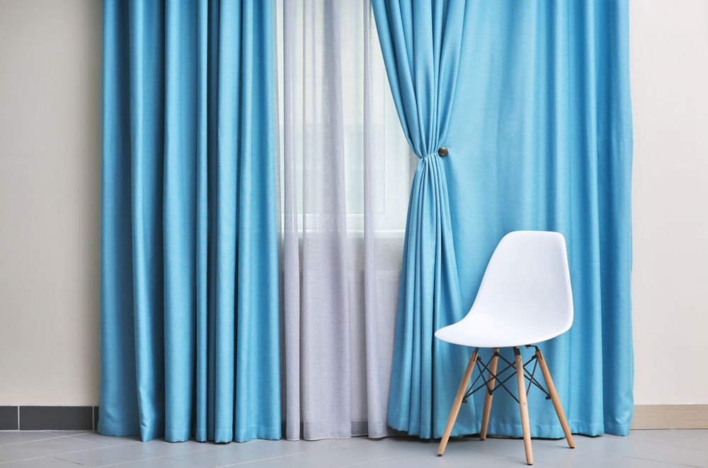 A White Chair is Sitting in Front of a Window With Blue Curtains — Catrina's Custom Curtains & Blinds in Toukley, NSW