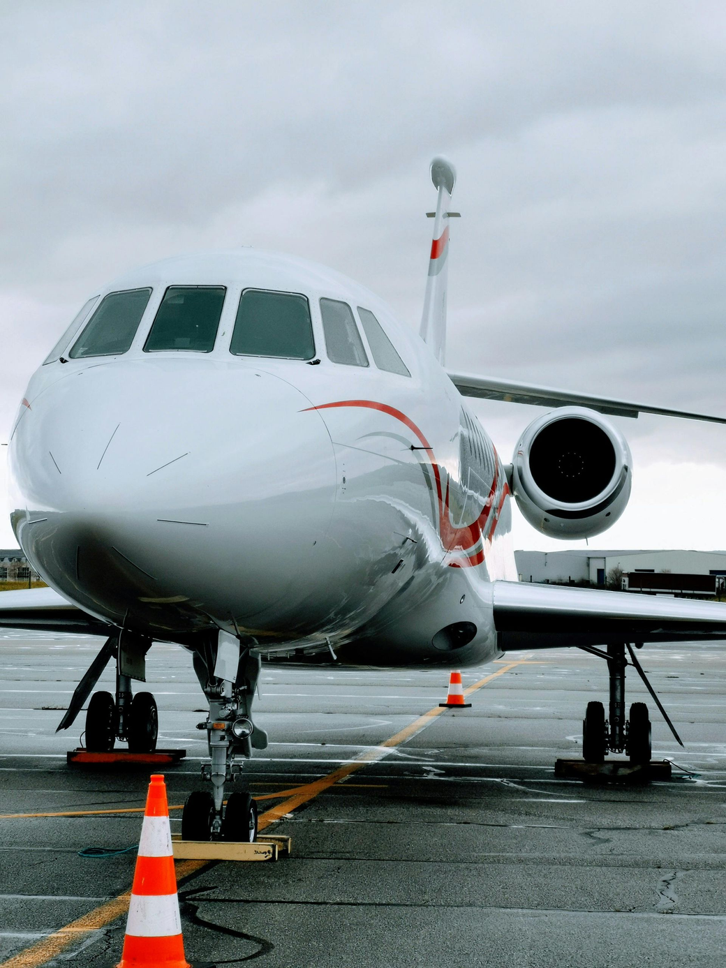 White private jet on a tarmac, orange stripe, cloudy sky, safety cone.
Jet Mentis Partners
