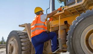 Un ouvrier du bâtiment grimpe sur un bulldozer.
