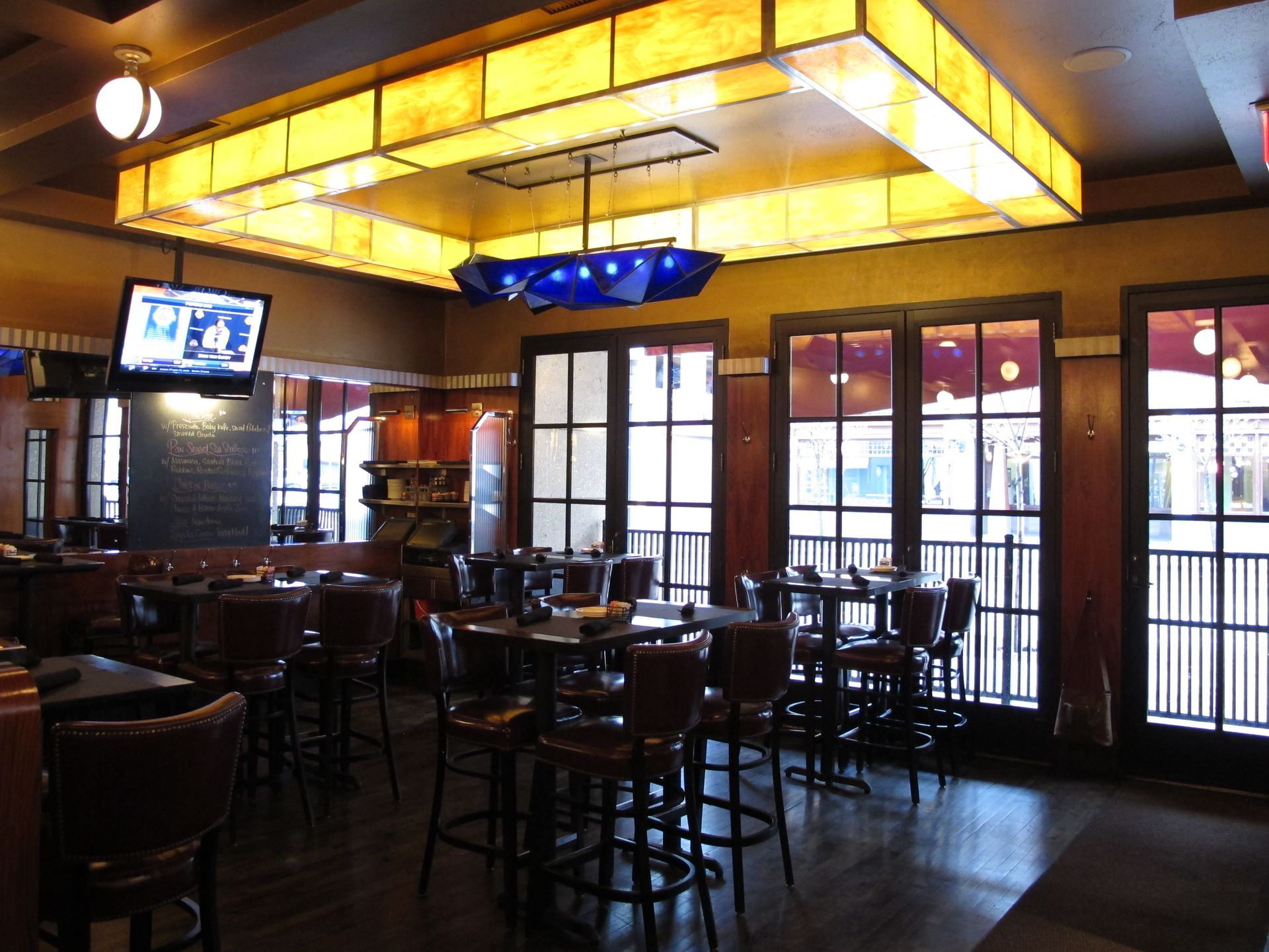 A dining room with tables and chairs and a tv hanging from the ceiling