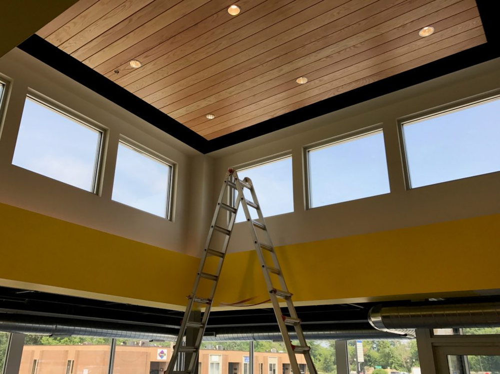 A ladder is sitting in a room with lots of windows and a wooden ceiling.