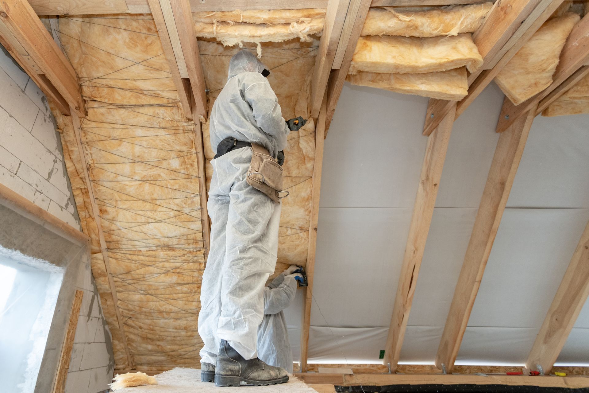 Two workers in protective suits insulating an attic with spray foam.