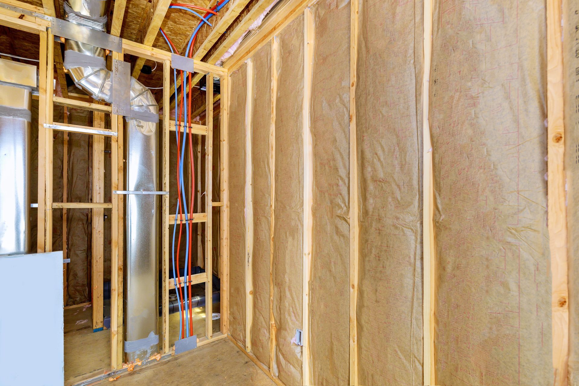 Interior wall framing with insulation, ductwork, and wiring installed in a new construction setting.