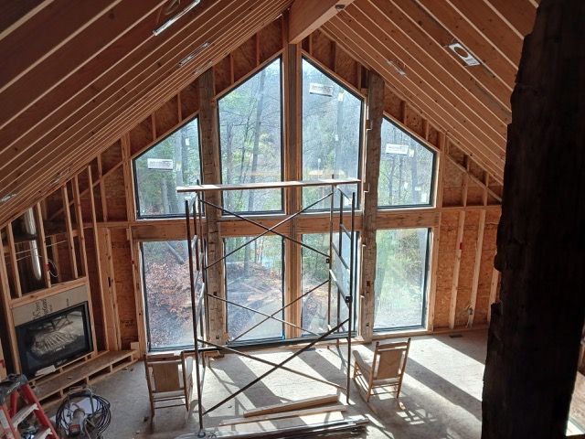 Interior of a wooden framed structure with large windows, unfinished construction. A scaffold is centered.