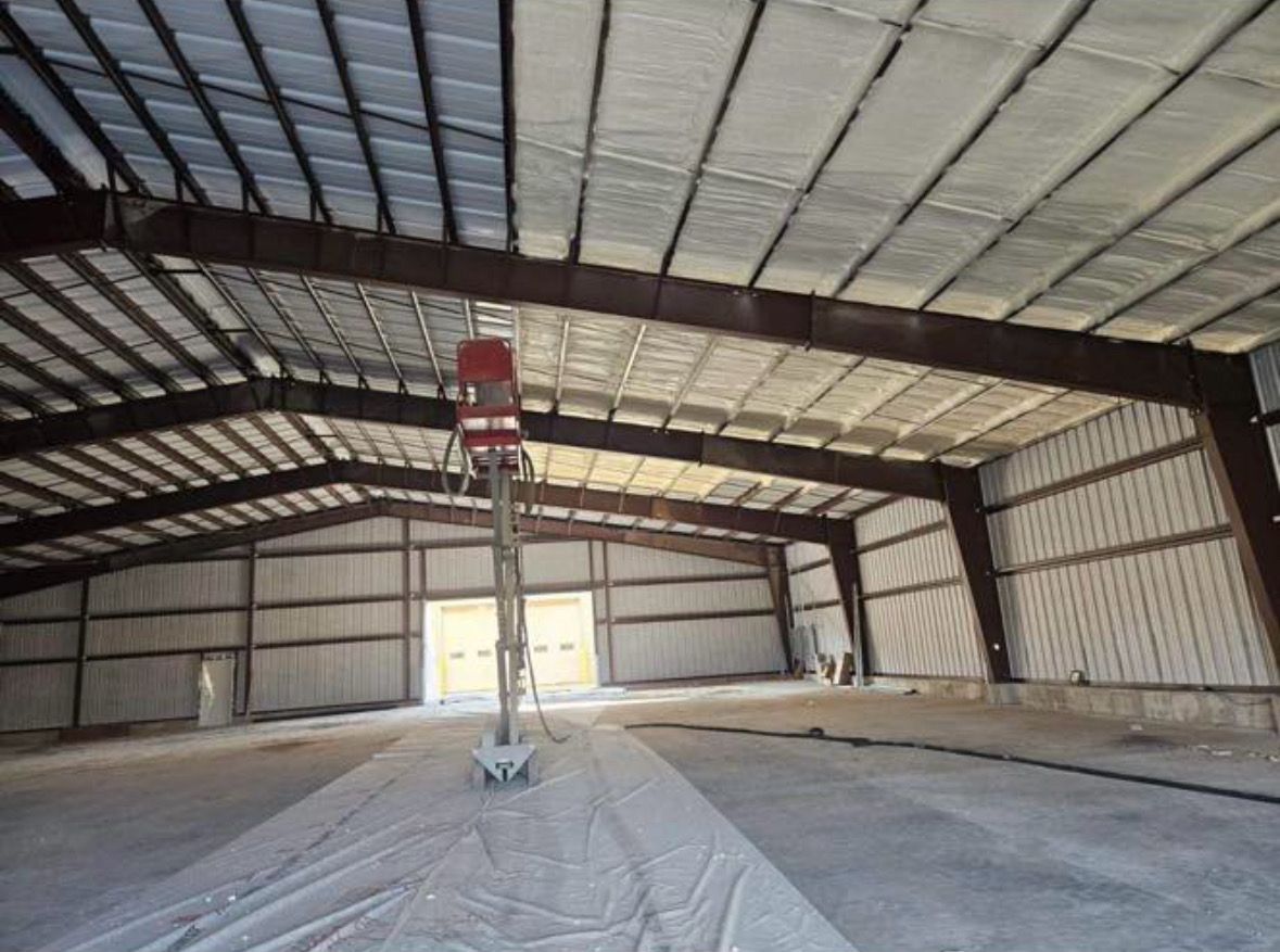 Interior of a large metal building with exposed beams, partially insulated ceiling, and a lift.