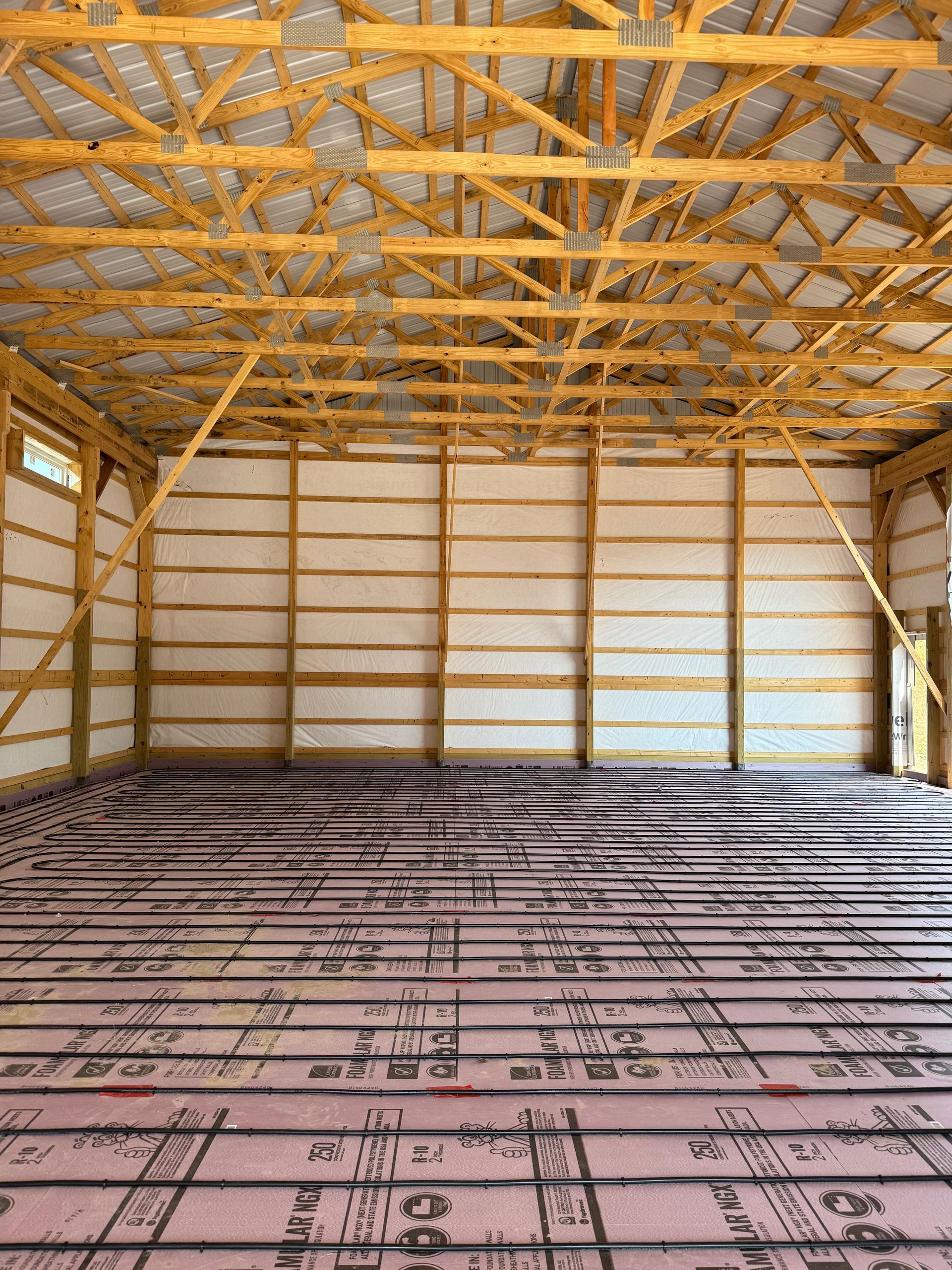 Interior of a partially constructed wooden building, with trusses, studs, and insulation visible.