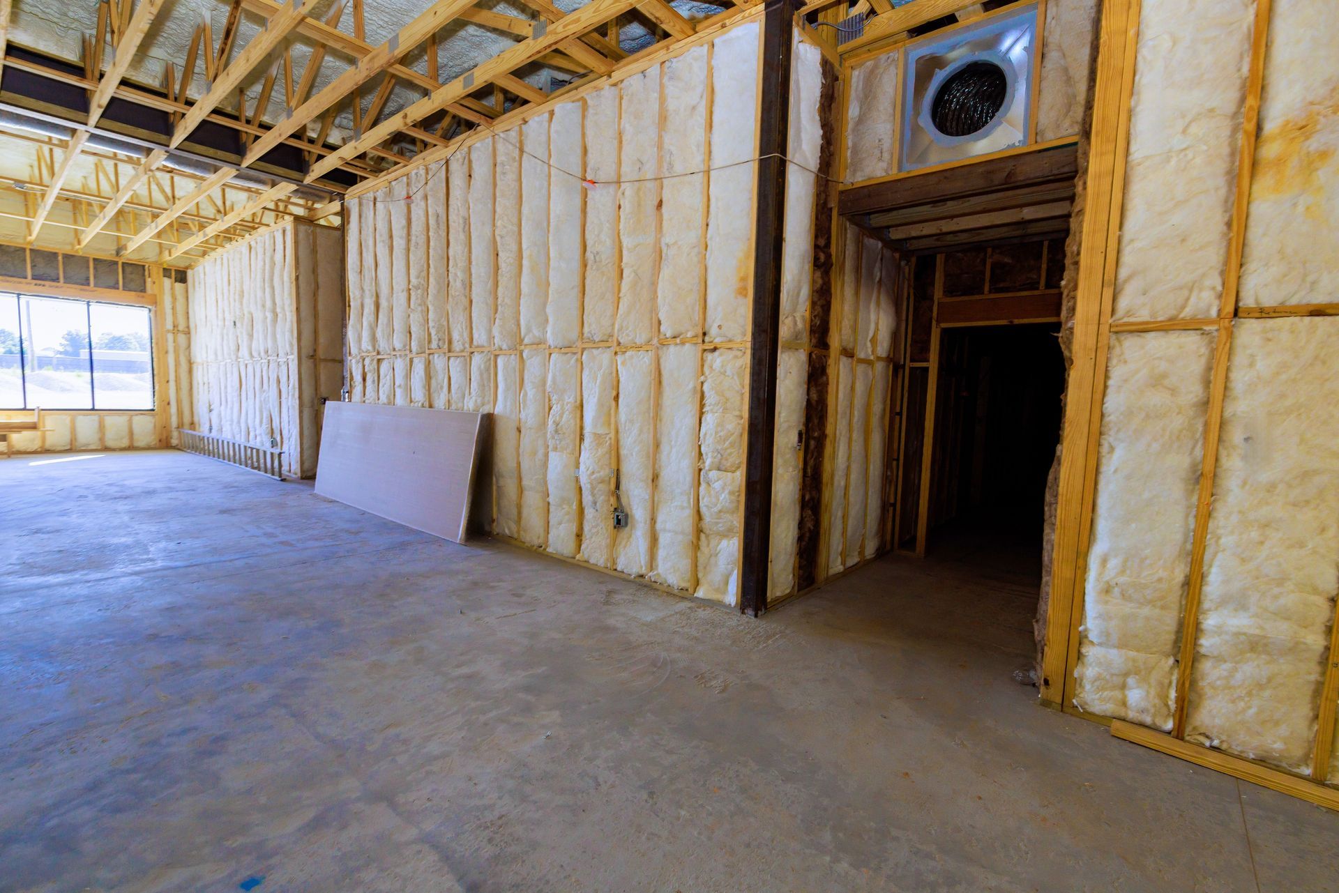 An unfinished room under construction, featuring exposed wooden beams, insulation-filled walls, and a concrete floor.