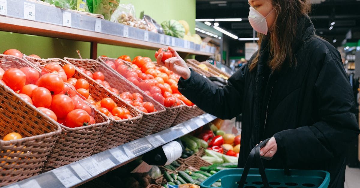 A woman wearing a mask is buying tomatoes in a grocery store.