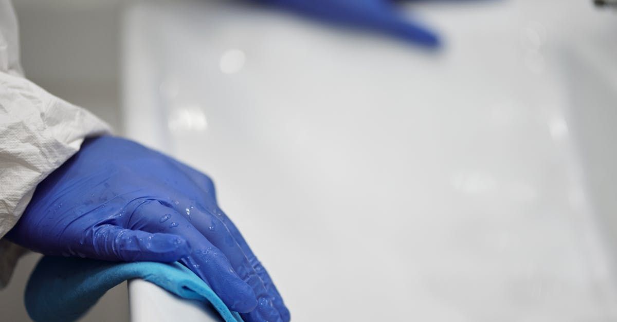 A person wearing blue gloves is cleaning a sink with a sponge.