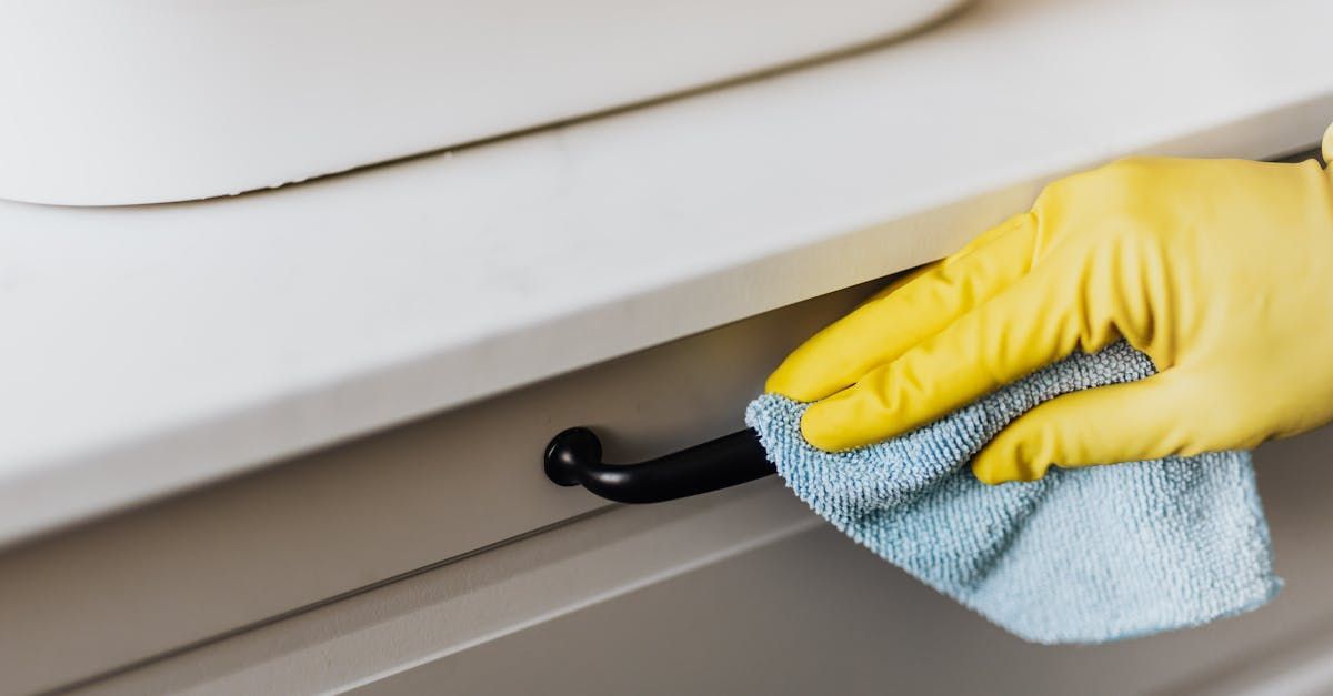 A person wearing yellow gloves is cleaning a cabinet with a towel.