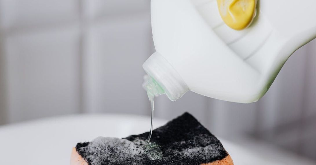 A bottle of dish soap is being poured on a sponge.