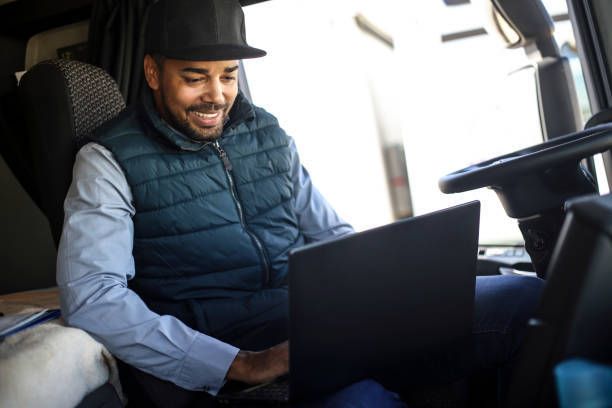 A man is sitting in the driver 's seat of a truck using a laptop computer.