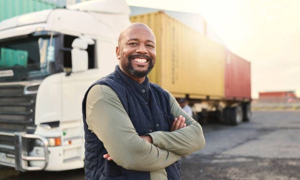 A man is standing in front of a semi truck with his arms crossed.