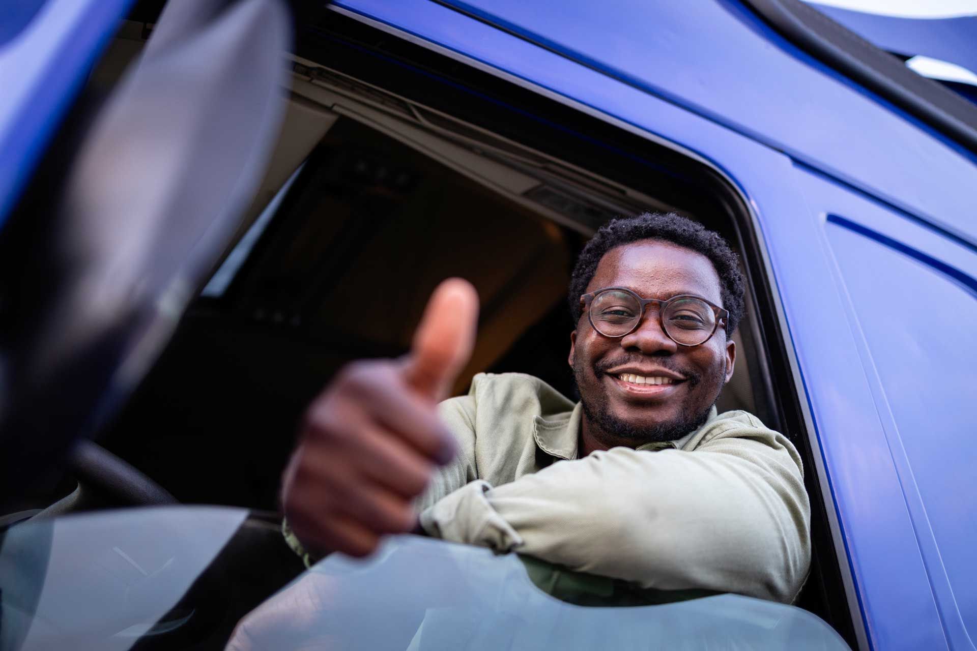 A man is giving a thumbs up while sitting in the driver 's seat of a truck.