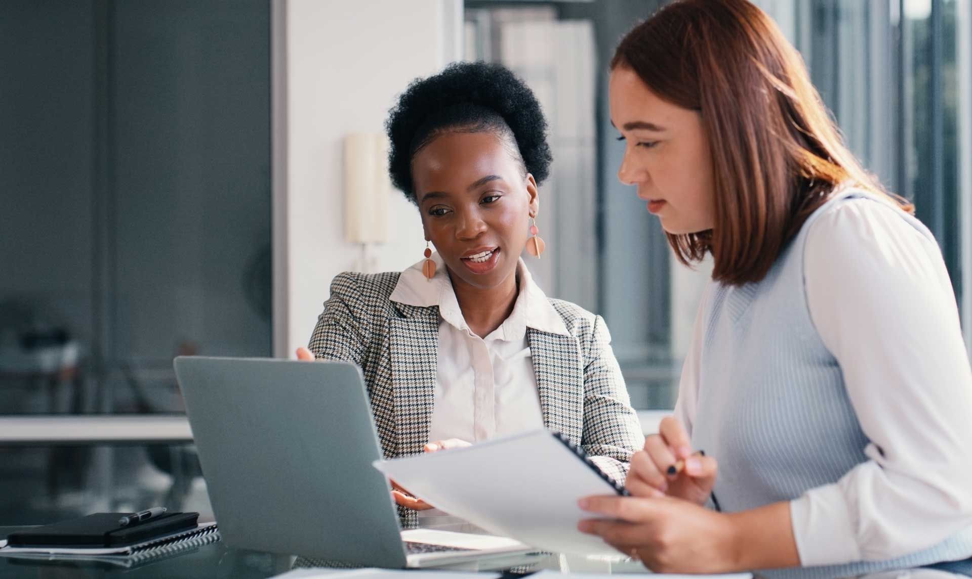Two women are sitting at a table looking at a laptop.