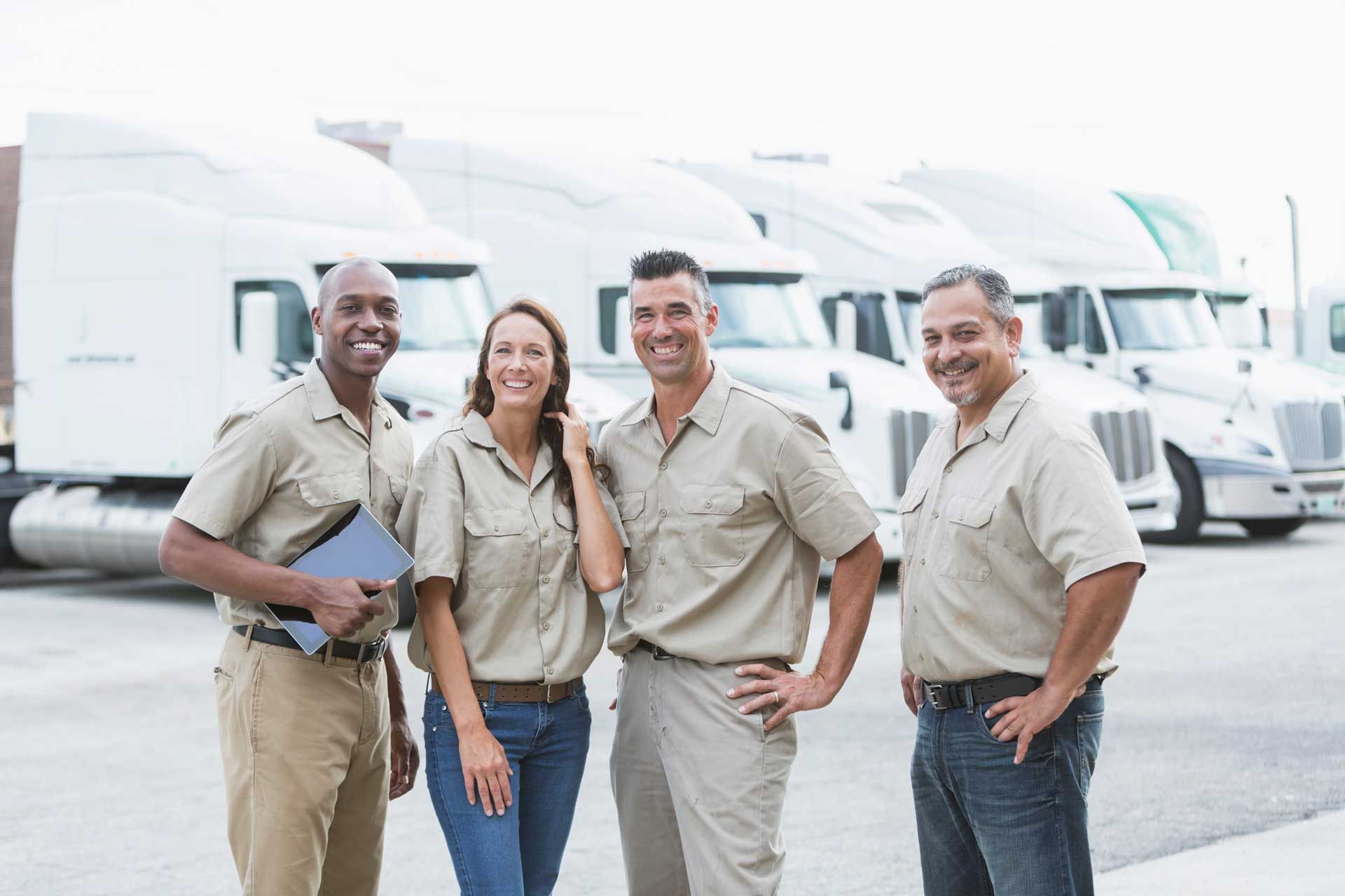 A group of truck drivers are posing for a picture in front of a row of semi trucks.