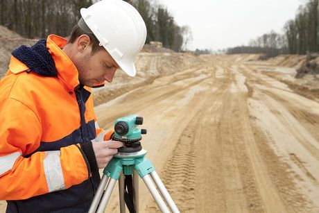 A man is using a level on a tripod on a dirt road near Houston, Texas