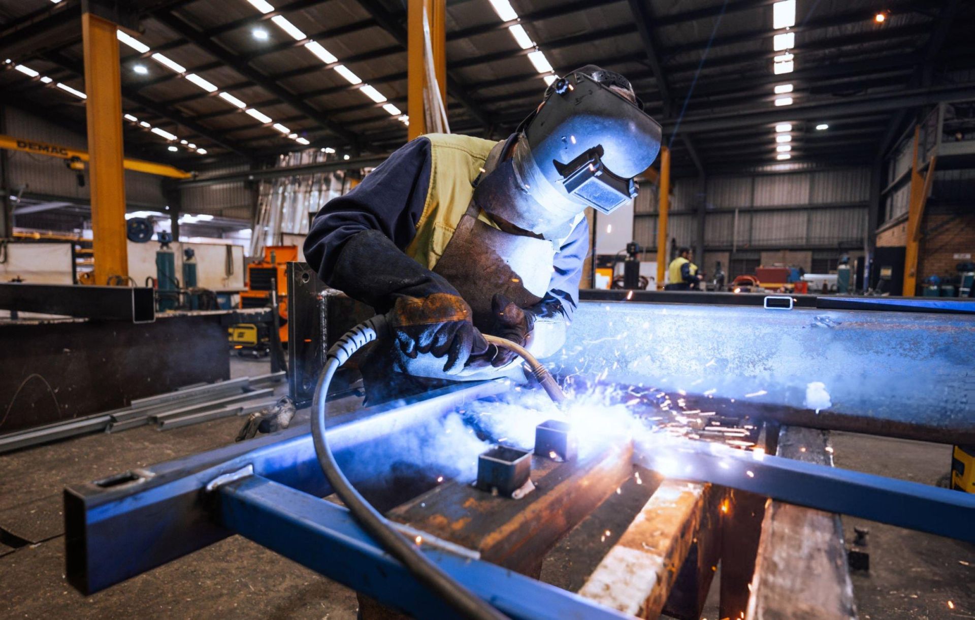A worker in protective gear welding metal in an industrial setting with sparks flying.