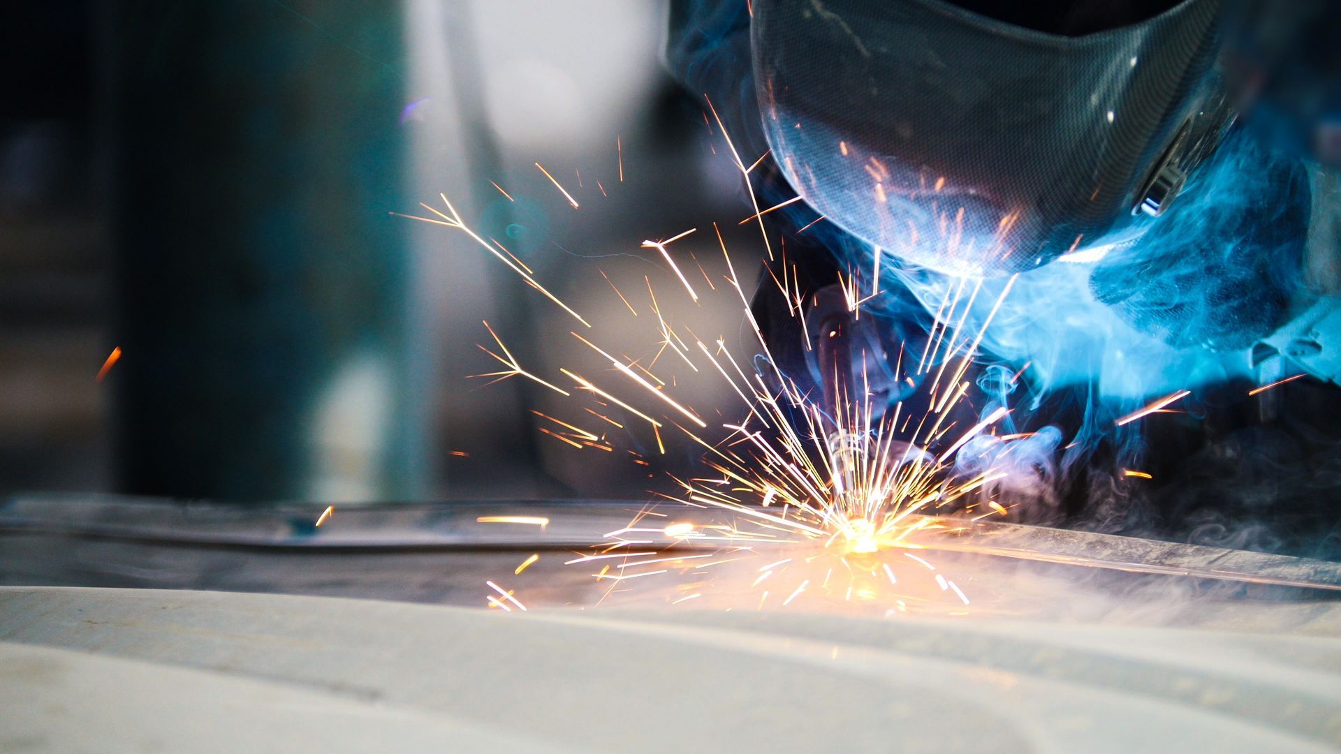 Close-up of welding sparks and smoke as a metal joint is welded on a flat steel surface.