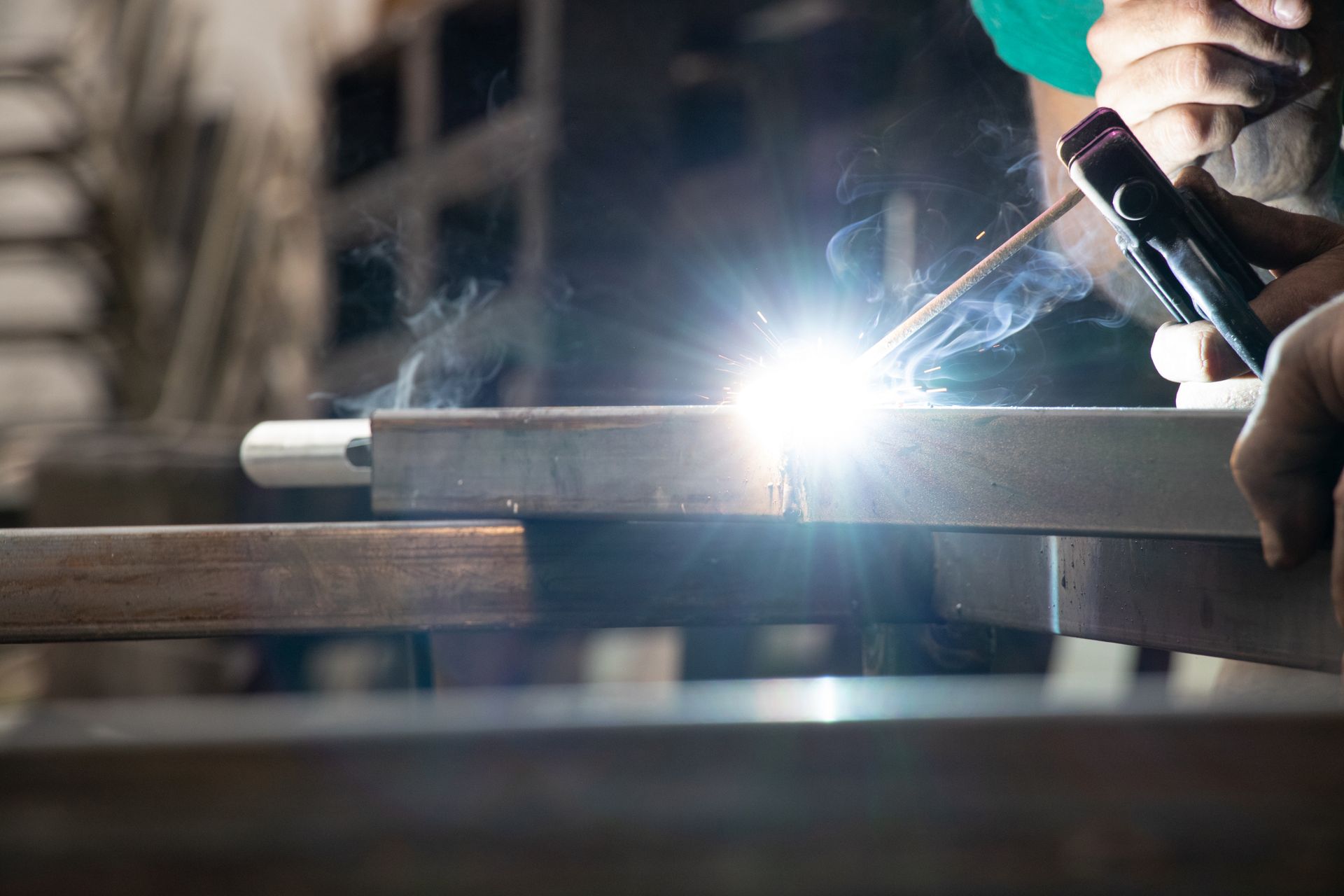 Close-up of welding sparks as a worker welds metal beams using an electrode holder.