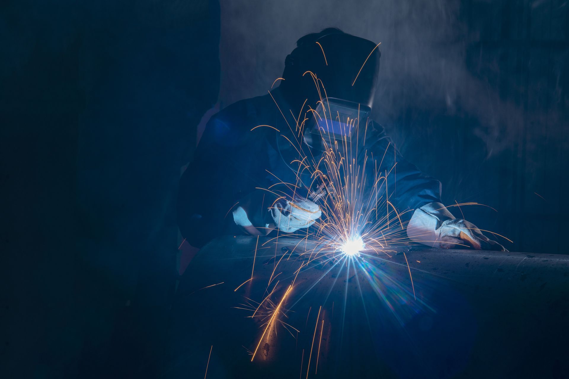 Welder creating bright sparks while working on metal in a dark workshop Welder creating bright sparks while working on metal in a dark workshop