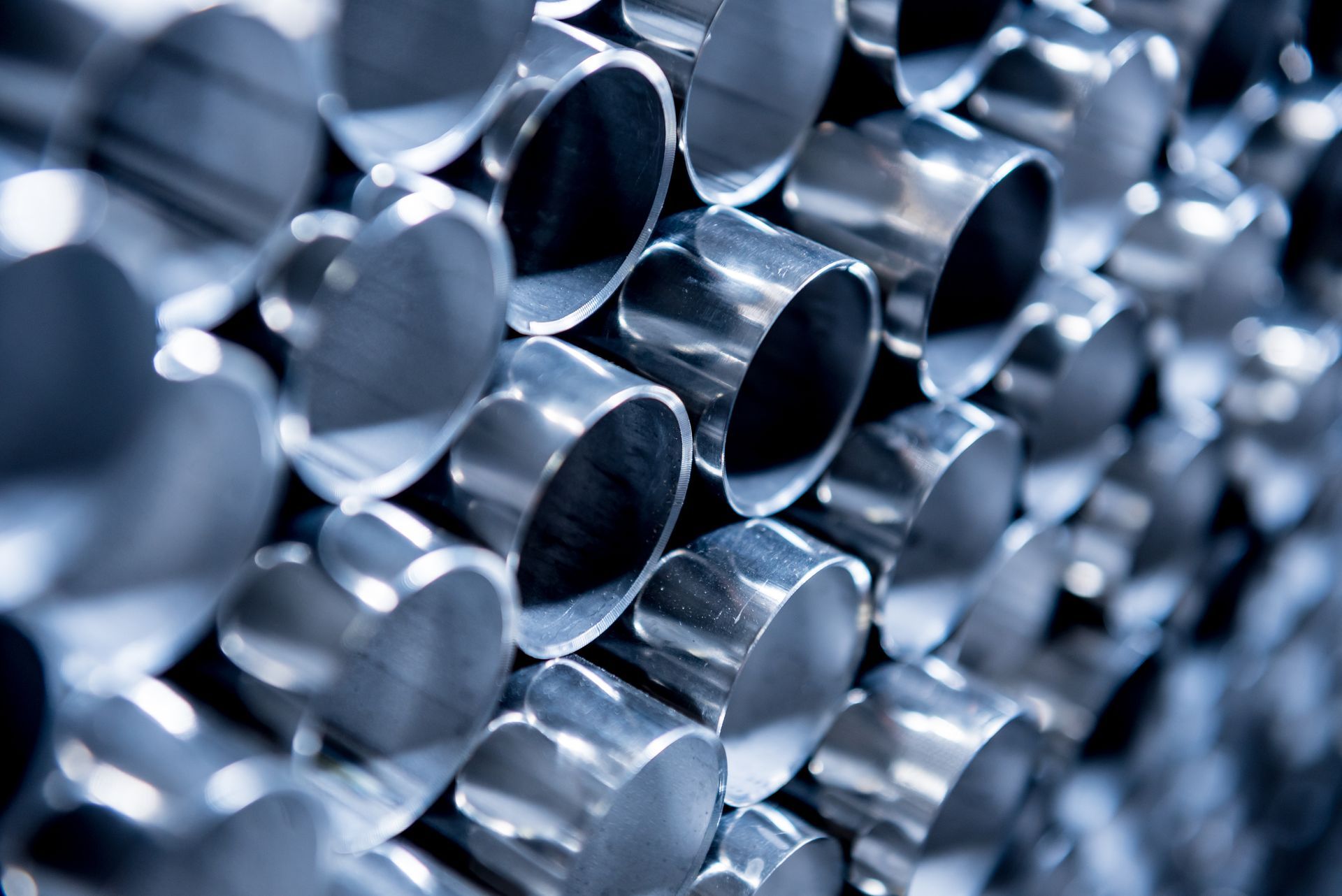 Stacked metal pipes or cylindrical steel tubes arranged closely together with reflective surfaces.