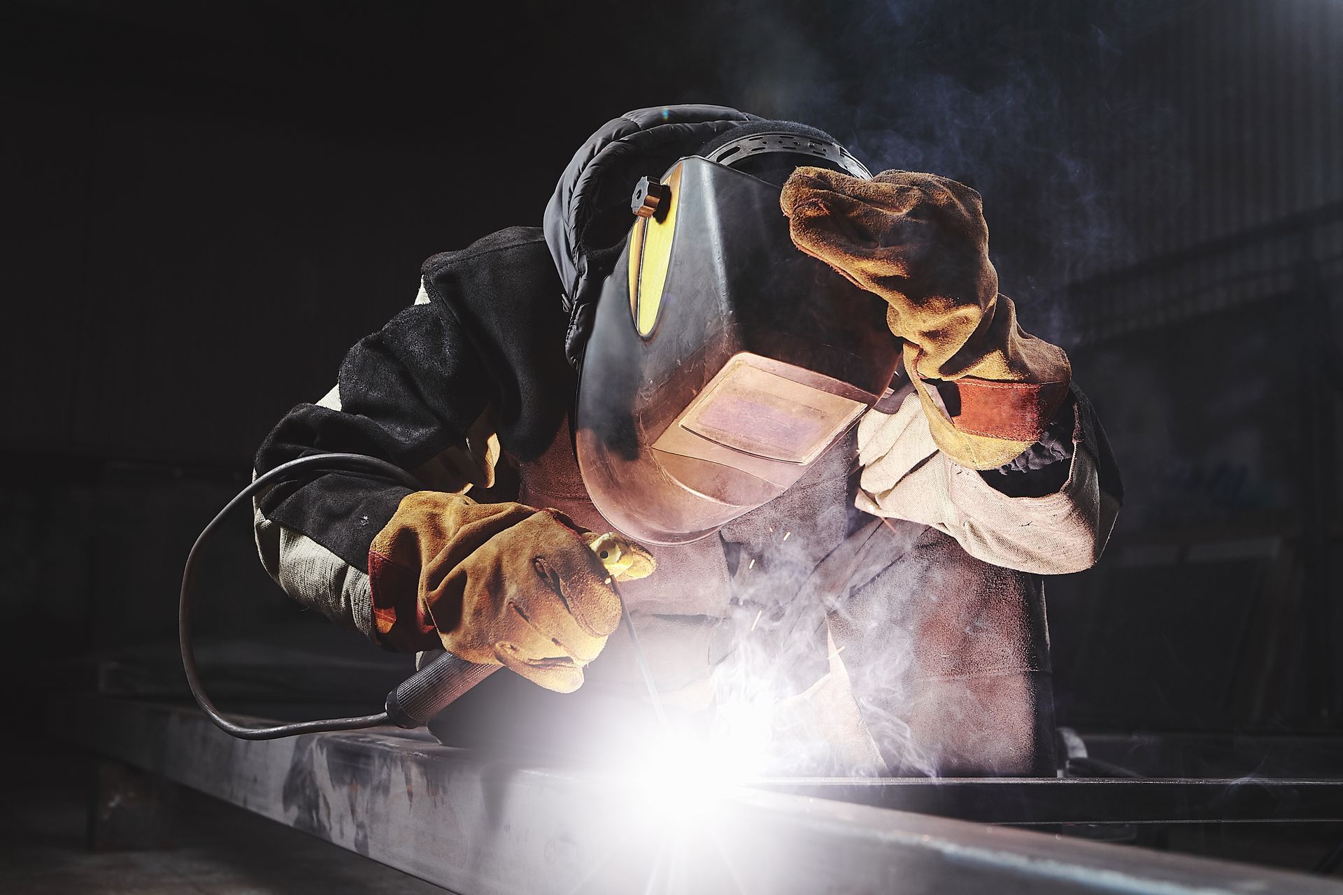 Professional welder performing welding services in protective gear with bright sparks visible.
