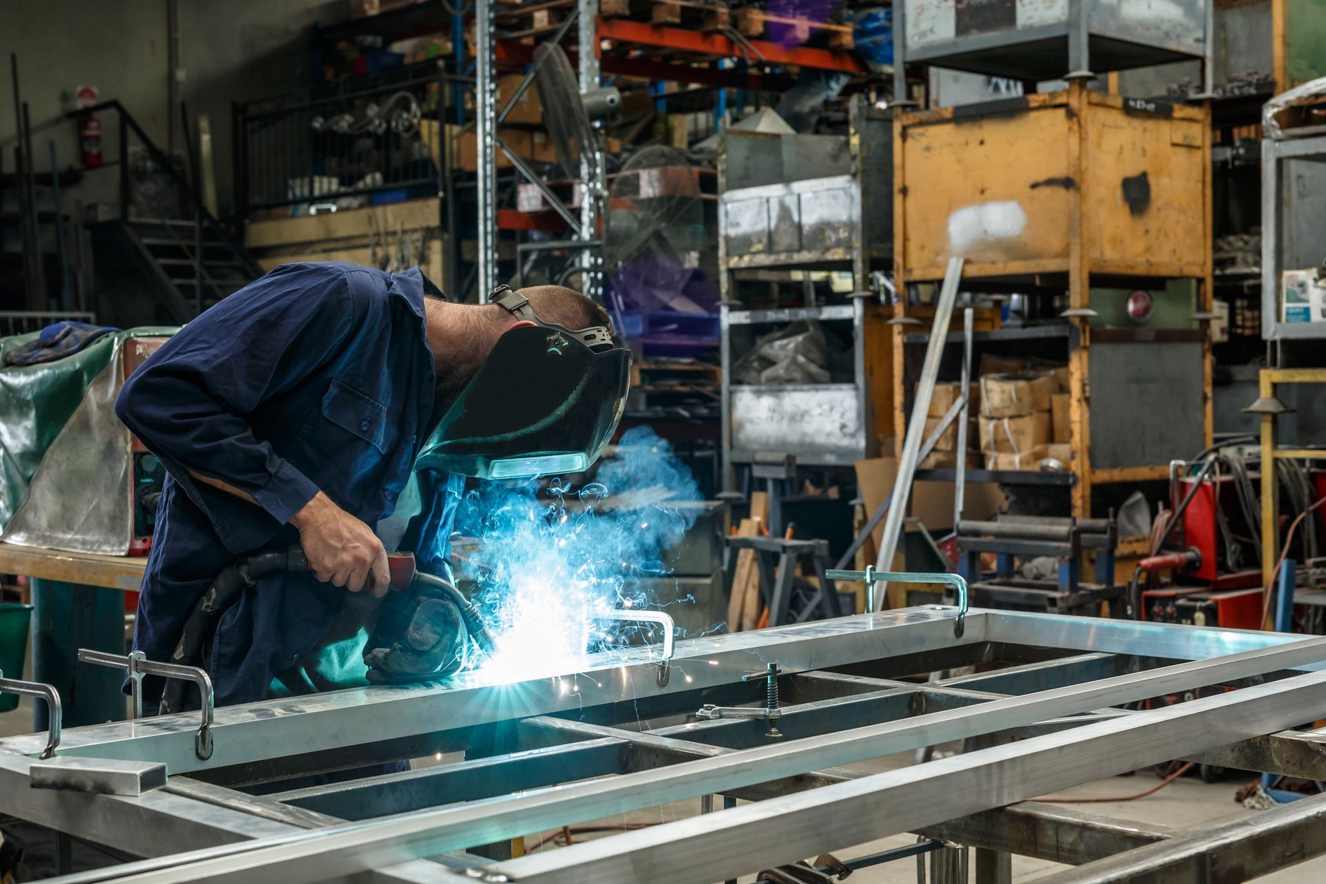Worker welding metal frame in an industrial workshop with bright sparks.