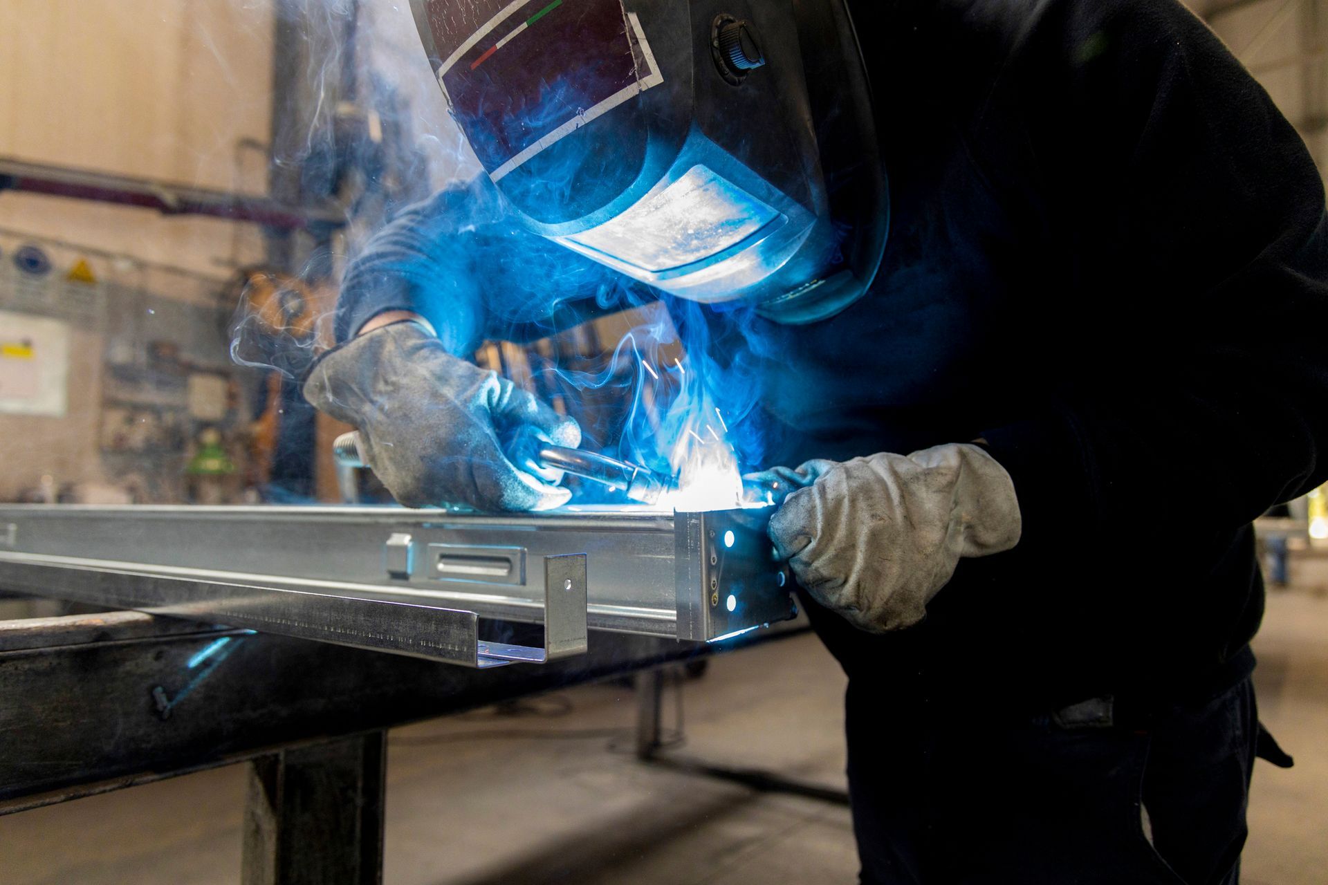 A person welding metal with protective gear in an industrial setting.