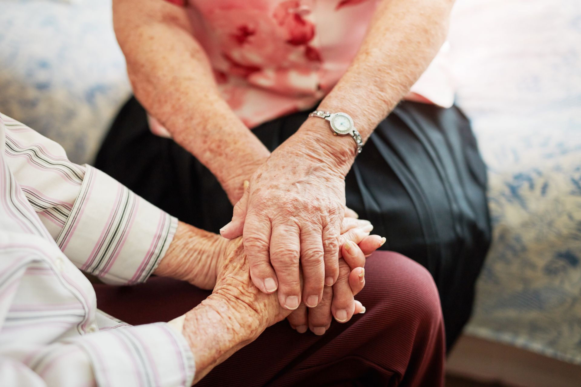 Two elderly women are holding hands while sitting on a bed.