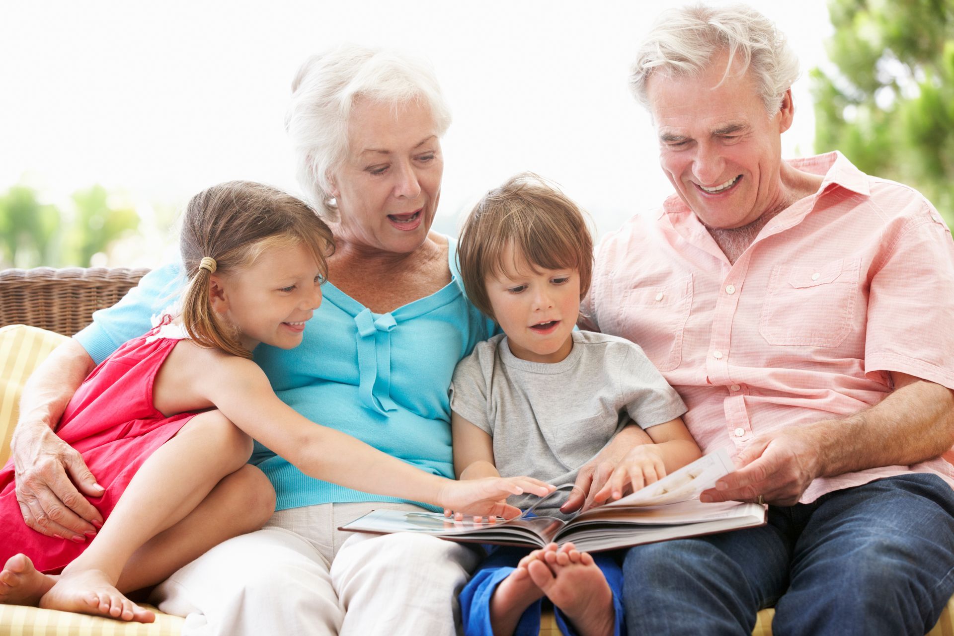 Grandparents with two grandchildren look at a book, smiling on a sunny day.