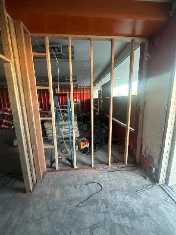 Construction site interior: framed wall, unfinished, showing exposed studs. Tools and materials visible.