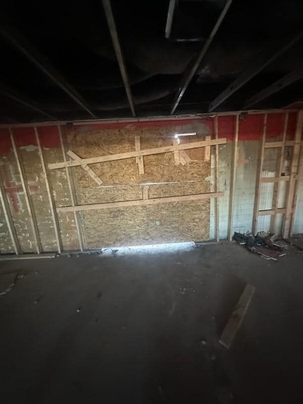 Interior room under construction, exposed wood framing, red top border, dark ceiling, concrete floor.