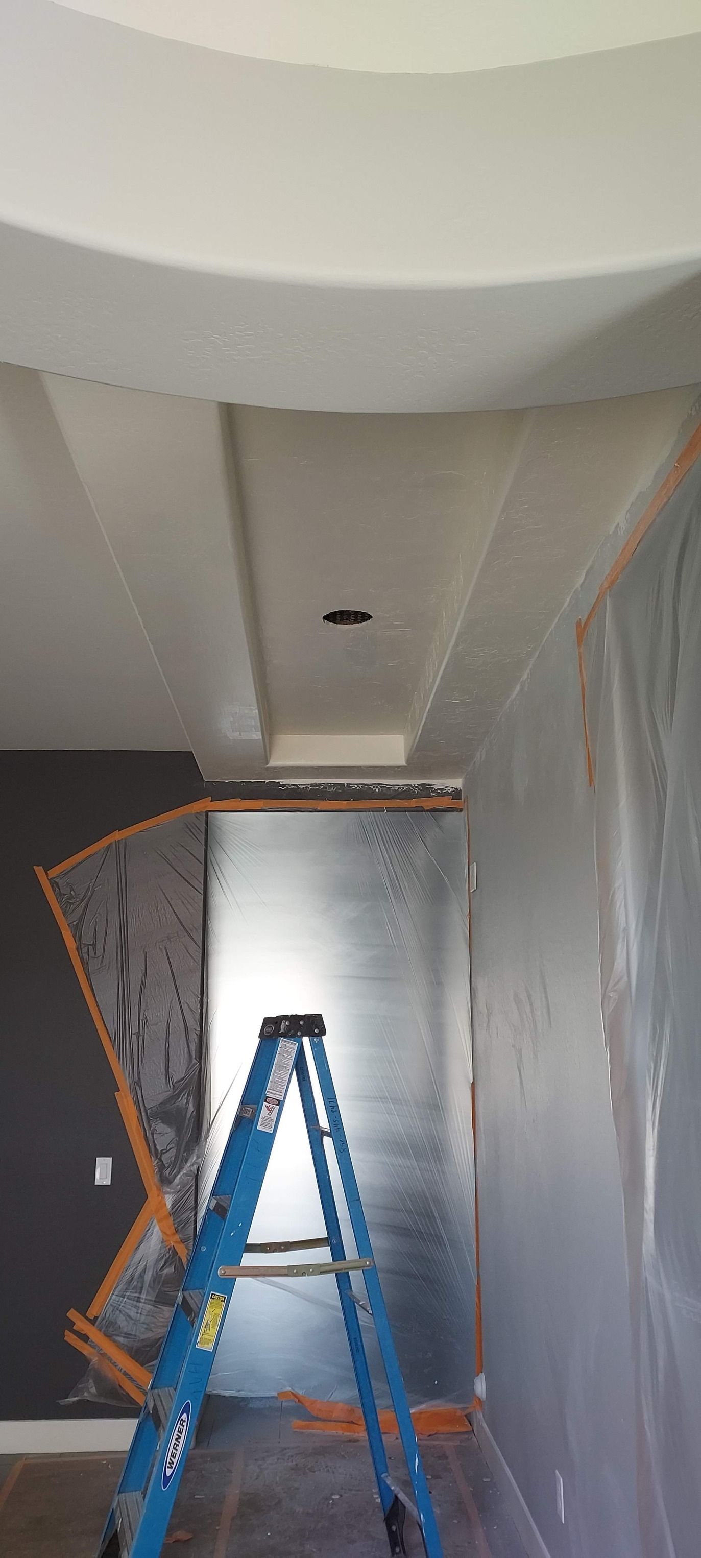A blue ladder in a room with plastic sheeting on the walls, likely during a renovation.