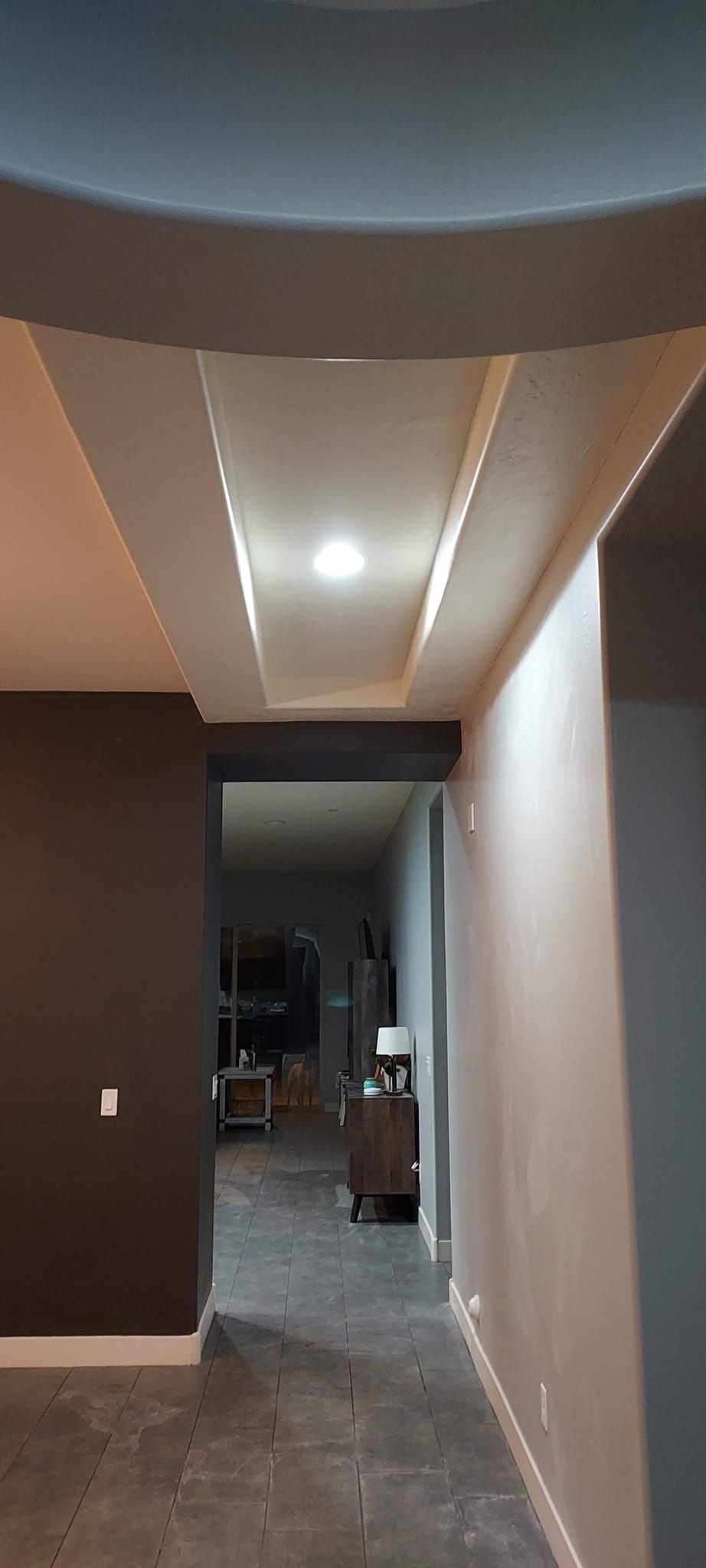 Hallway with a coffered ceiling and recessed lighting. Dark and light walls with a concrete floor.