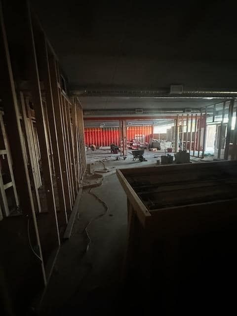 Interior construction site with exposed wooden framing, orange wall, and debris.