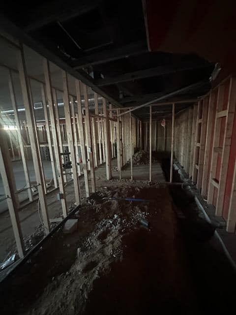 Interior view of a building under construction, showing exposed wooden studs and debris.