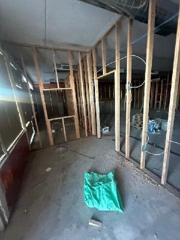 Construction site: Wooden wall frames in a room with concrete floor, green bag, and wiring.