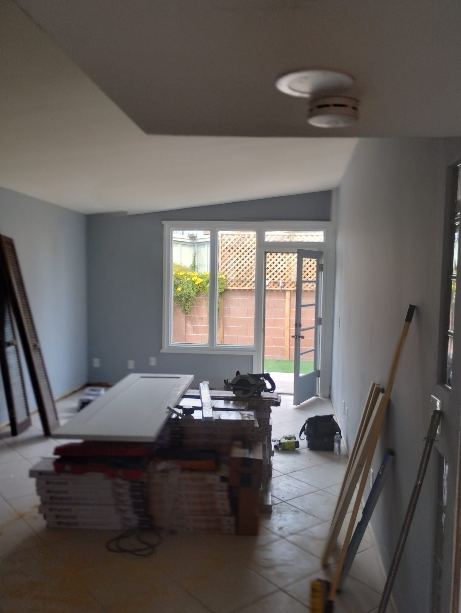 Room under construction with tools, materials, and open door leading to a backyard.