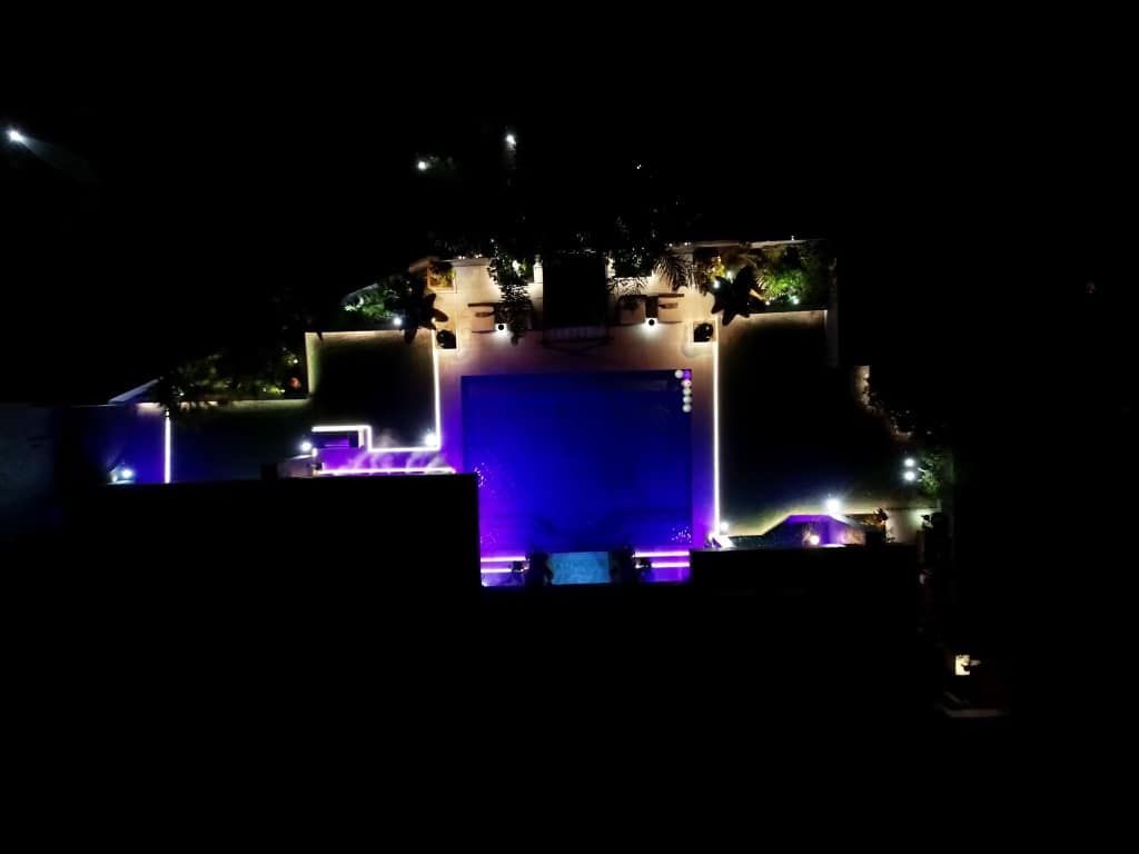 Nighttime aerial view of a venue with a large blue screen and lit seating areas.