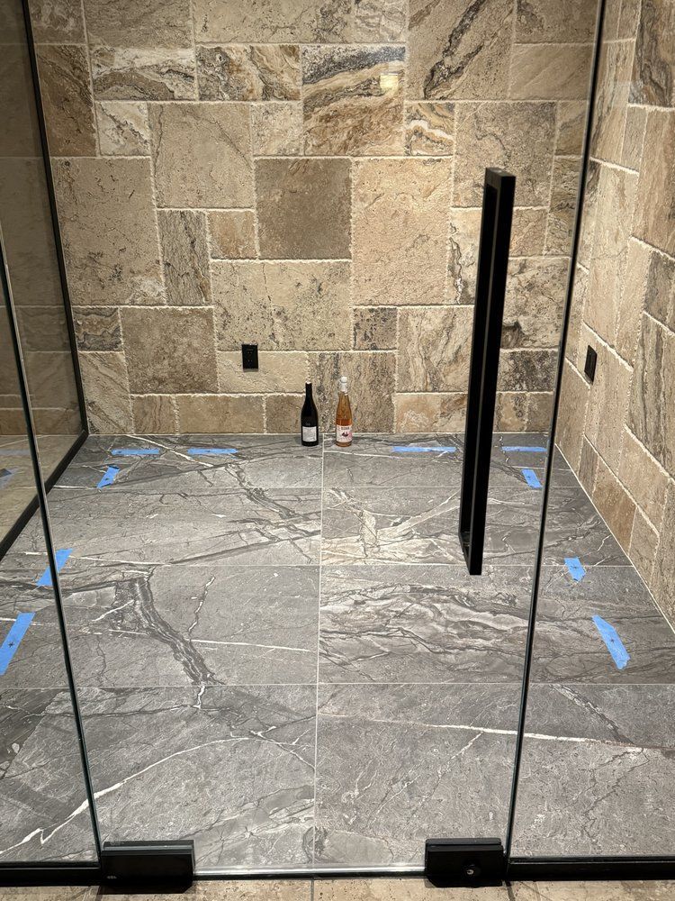 Shower with glass doors, tiled walls and floor.  Black handle and hinges. Two bottles on the floor.