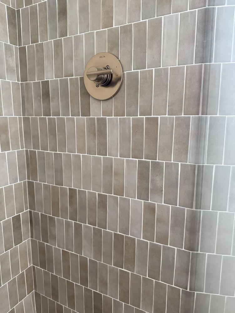 Shower interior with rectangular, gray-brown tiles and a silver faucet control.