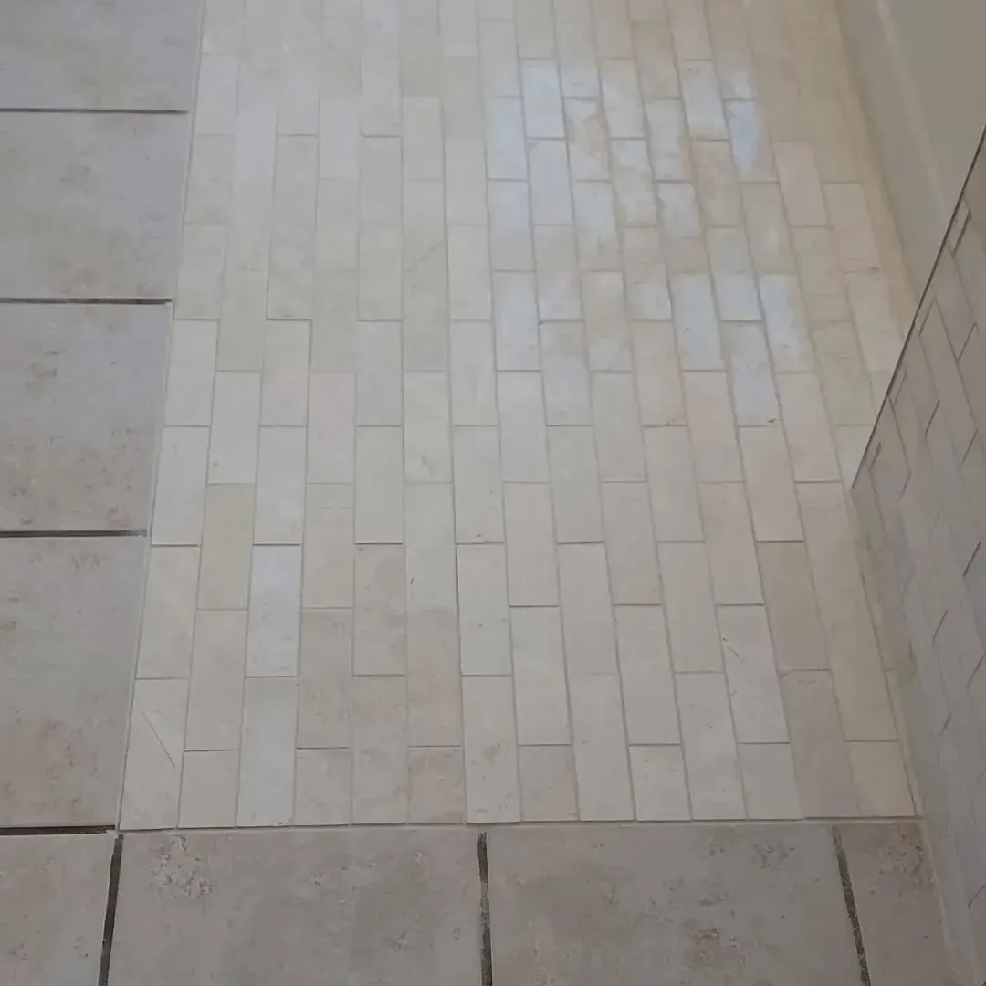 Light-colored rectangular tile flooring, in brick pattern, transitions to square tiles.