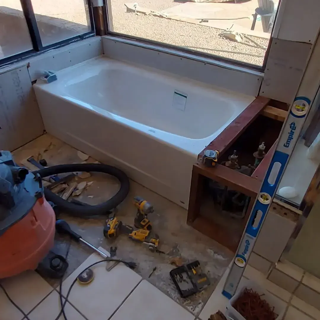 Bathtub installation in progress; tools and construction debris scattered in a bathroom with a large window.