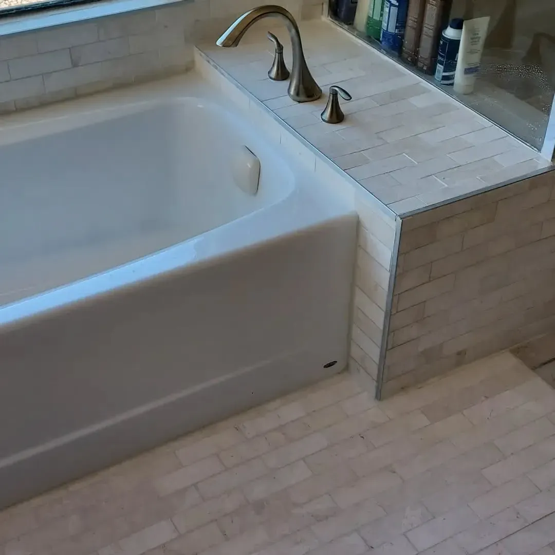 Bathtub with brass fixtures and stone tile surround and floor.