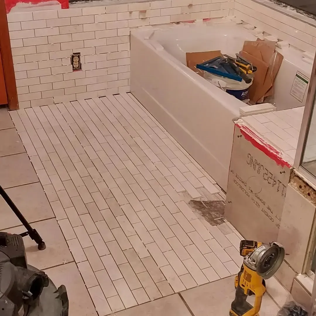 Bathroom under renovation, floor tiled with white subway tiles. Tub and partial wall in view, tools present.