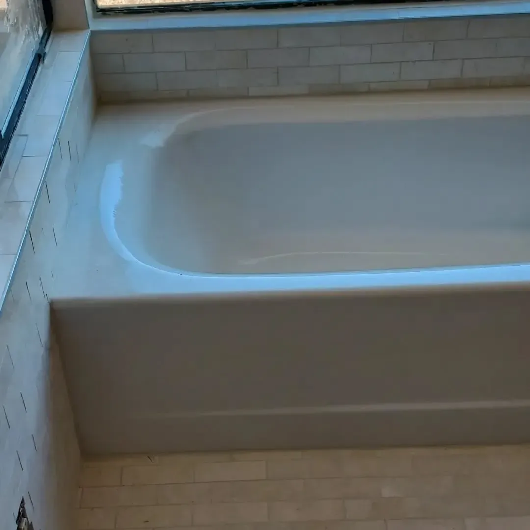 White bathtub, set in tiled alcove, beneath a window.