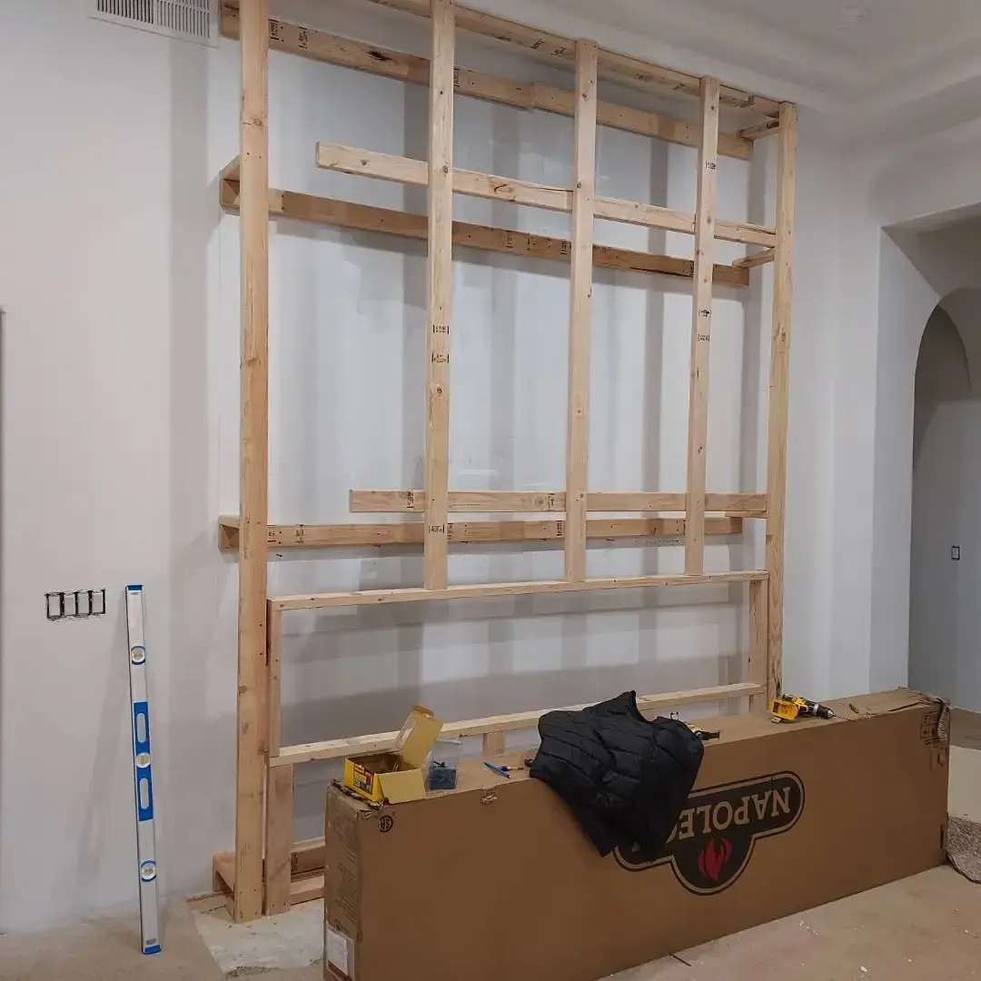 Wooden frame constructed against a white wall; a box, level, and tools are present.