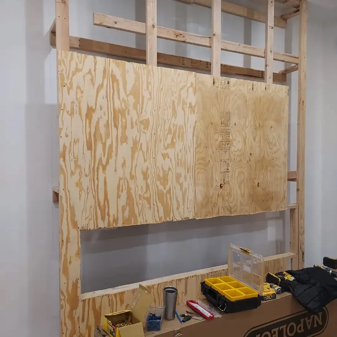 Wooden framework with plywood attached to a wall. Construction tools are in the foreground.